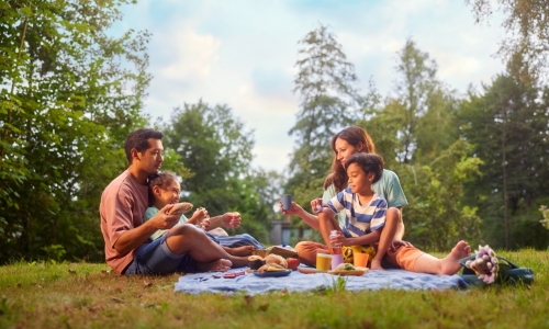 Une famille déjeune sur l'herbe à quelques mètres de leur cottage.